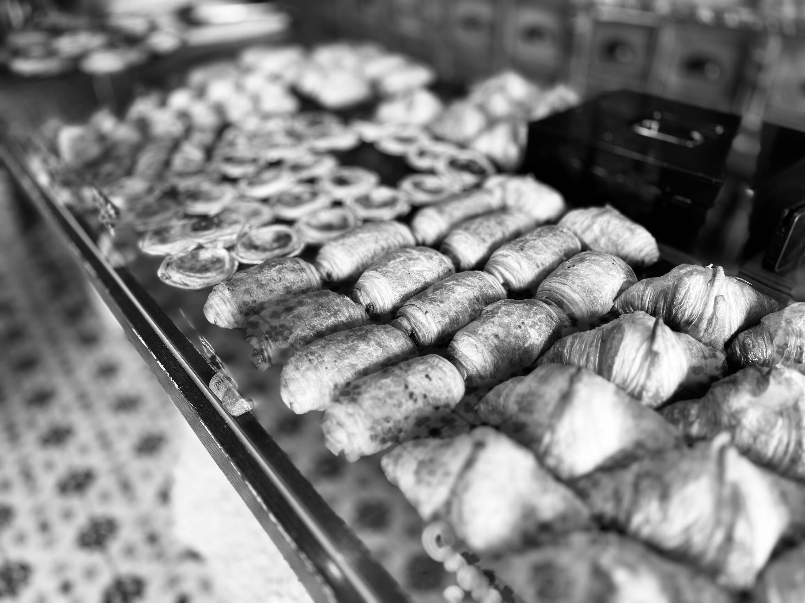 Auslage einer Bäckerei: Reihen von Croissants, Strudel und Plundergebäck hinter Glas.