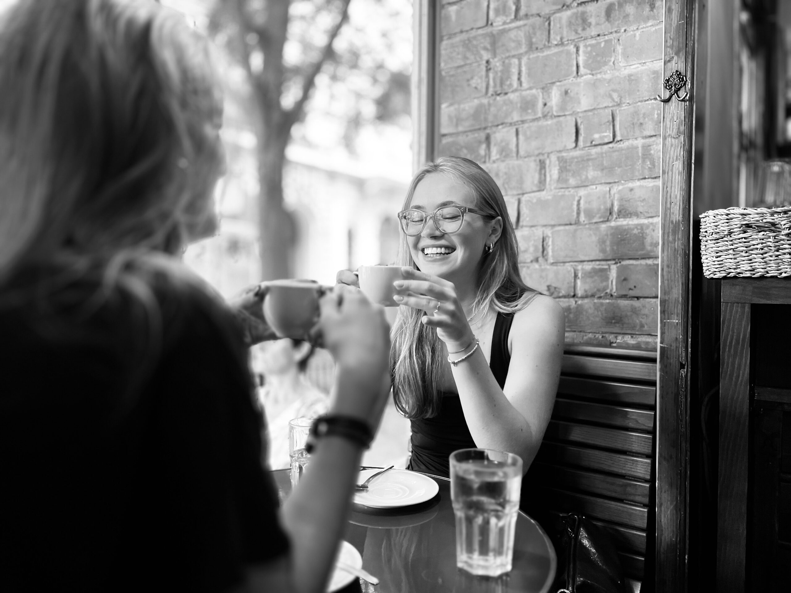 Zwei Frauen an einem Kaffeehaustisch im Freien, eine hält die Tasse in beiden Händen.