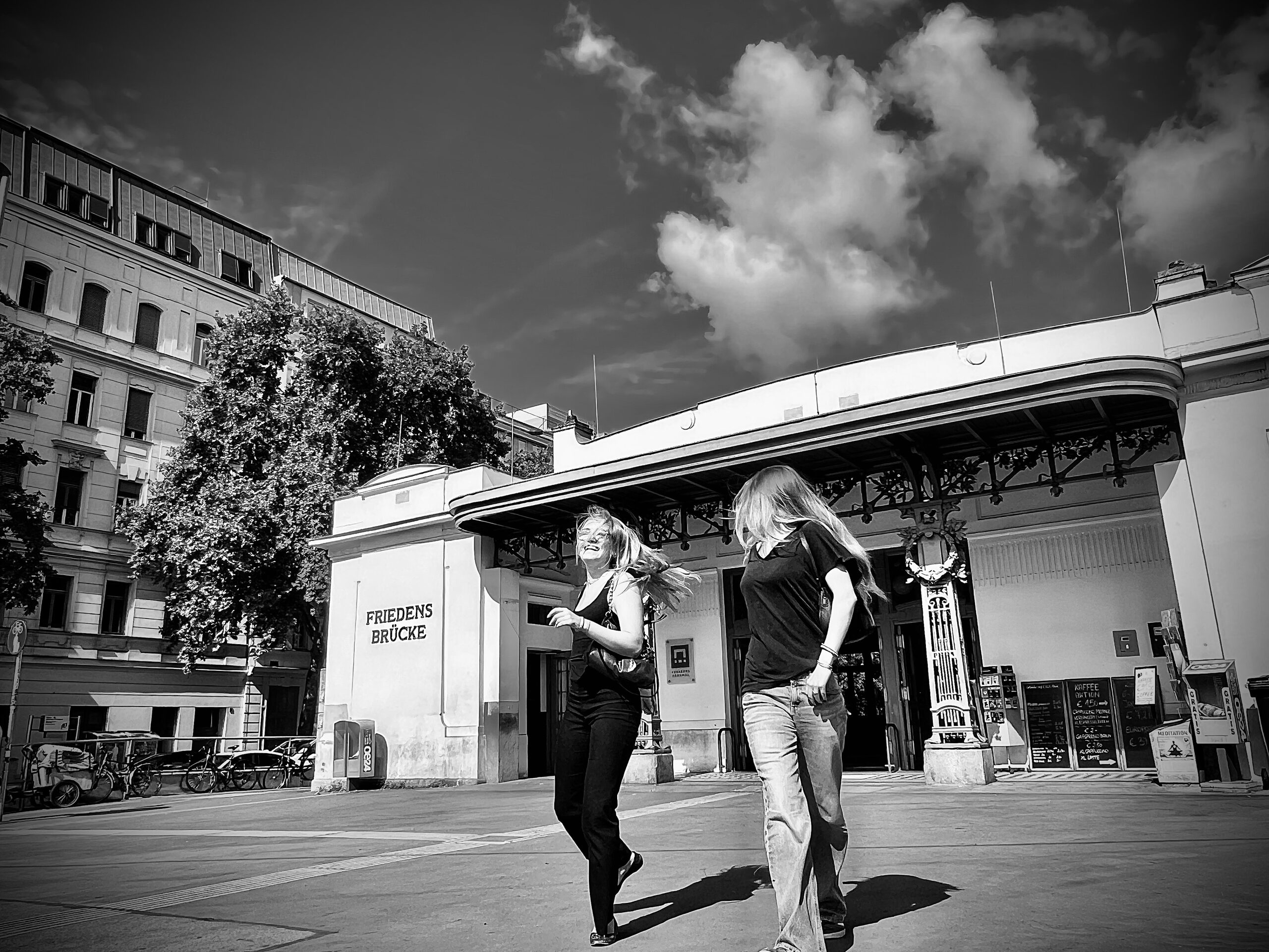 Am Stationsgebäude Friedensbrücke: zwei Frauen davor, darüber ein bewölkter Himmel.