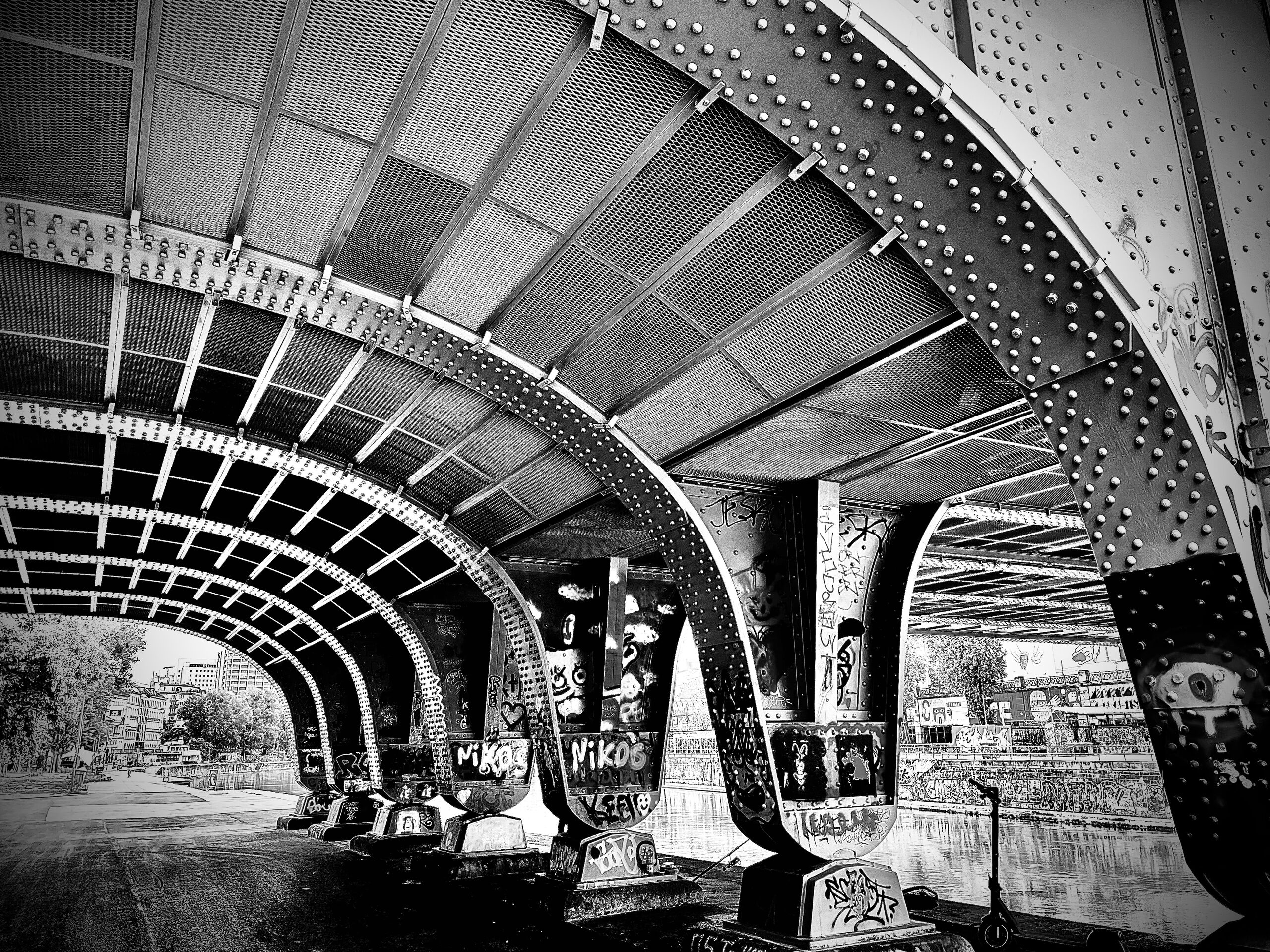 Unter der Brücke: genietete Stahlbögen, besprühte Pfeiler und der Weg am Kanal.